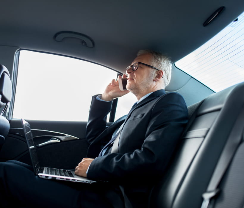 Businessman working on a laptop and smartphone in a luxury car.