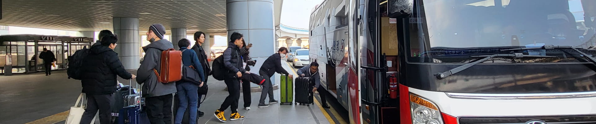 Passengers loading luggage onto an airport bus at a terminal.