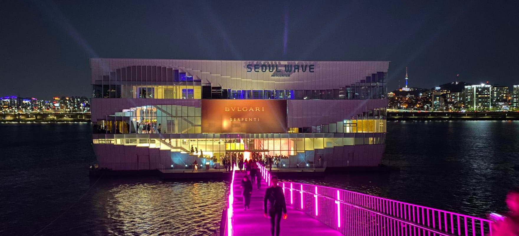 Night view of the Seoul Wave Art Center with a Bvlgari Serpenti event, illuminated entrance, and cityscape in the background.