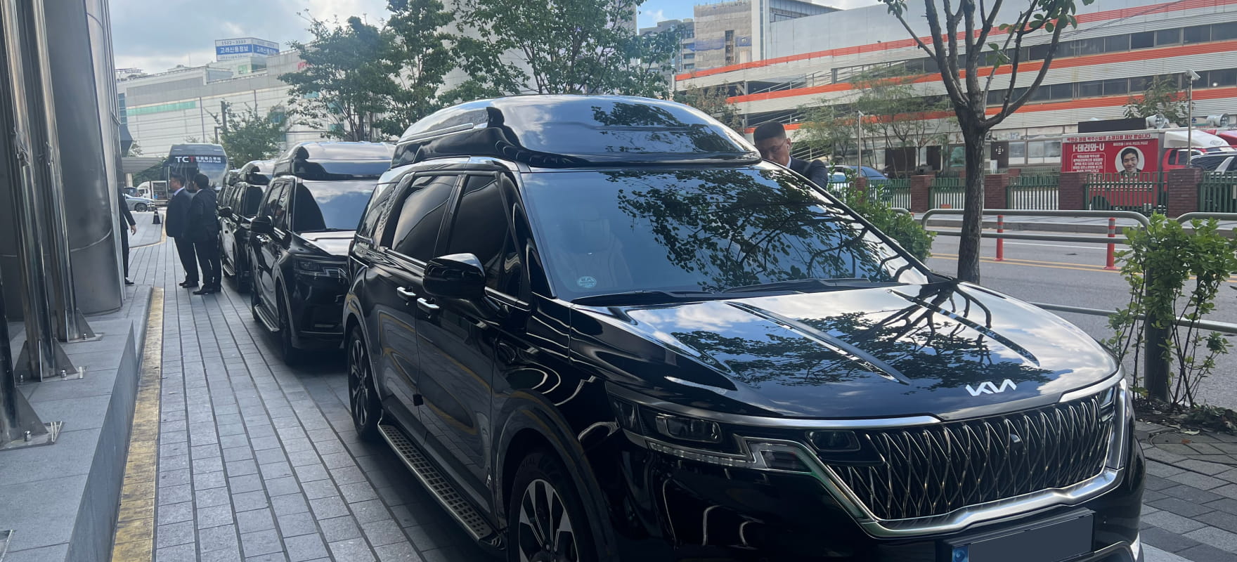 A long row of black Kia Carnival Hi-Limousine vans with roof boxes parked on a street for the 2024 Seoul International Drama Awards protocol service.