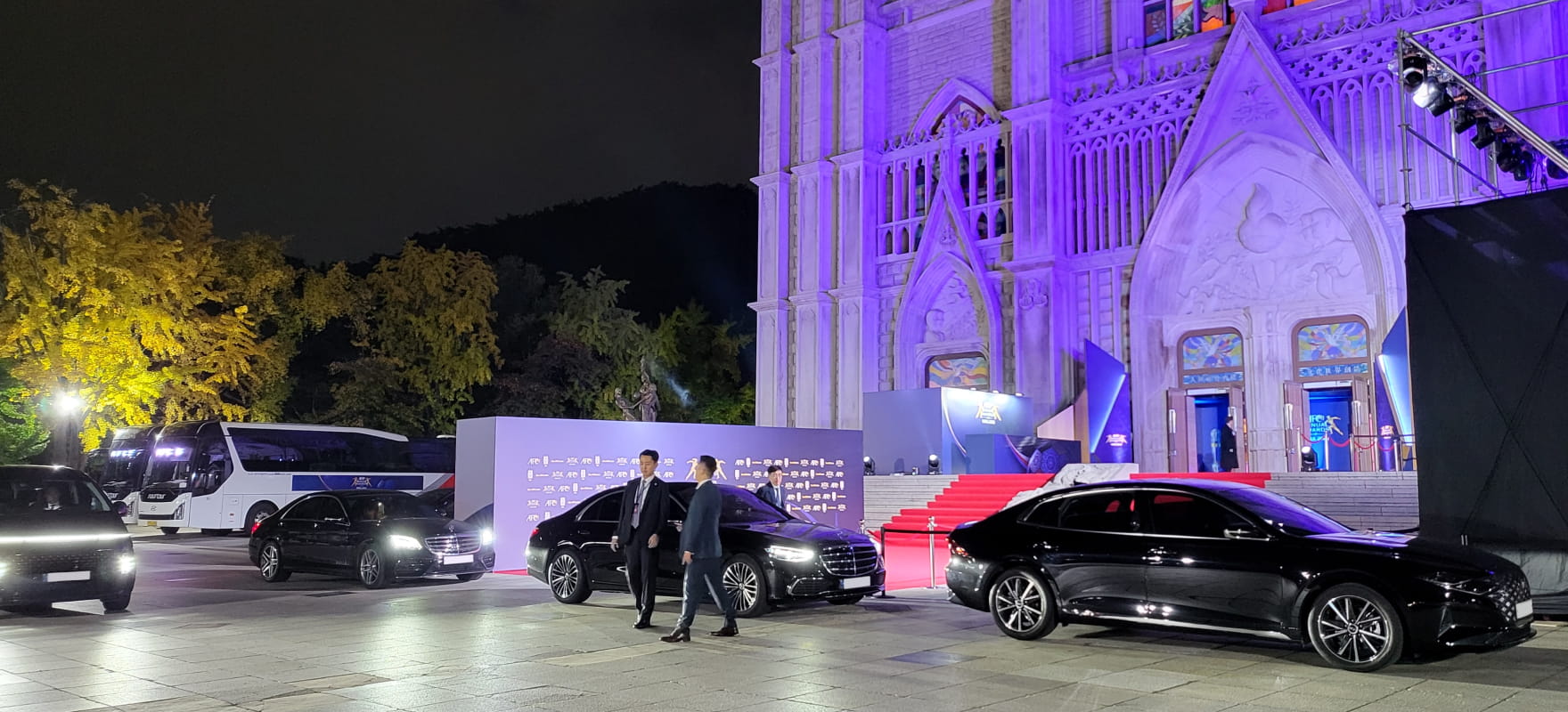 Professional chauffeurs standing by black luxury sedans at the red carpet entrance of the AFC Annual Awards 2023.