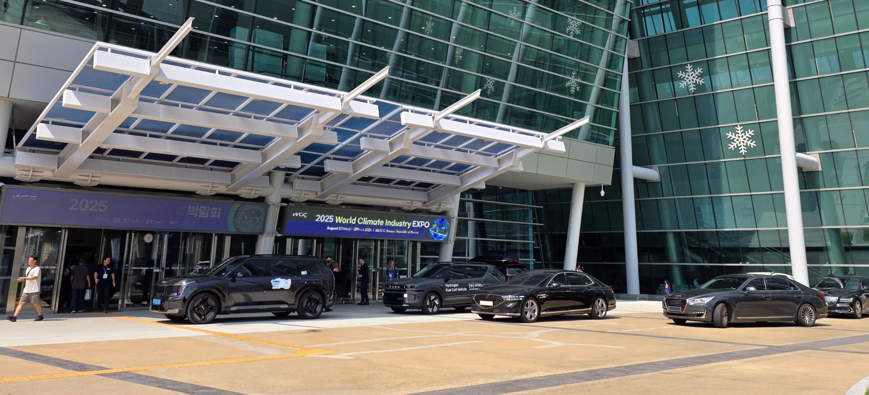 A fleet of black premium vehicles, including Genesis G90 and Kia EV9, parked at the BEXCO entrance for the 2025 APEC Energy Ministerial Meeting.
