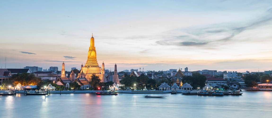 Wat Arun temple glowing at sunset along the Chao Phraya River, great for cultural tours.