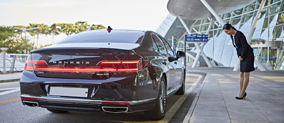 Professional concierge bidding farewell next to a luxury car at the airport, highlighting premium chauffeur services.