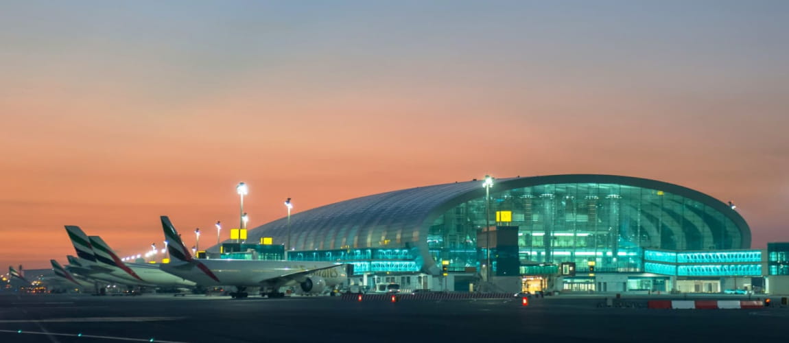 Dubai International Airport with Emirates planes at dusk, showcasing modern global travel.