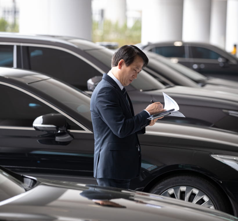 Black luxury sedans parked in a row, with a professional chauffeur checking documents.