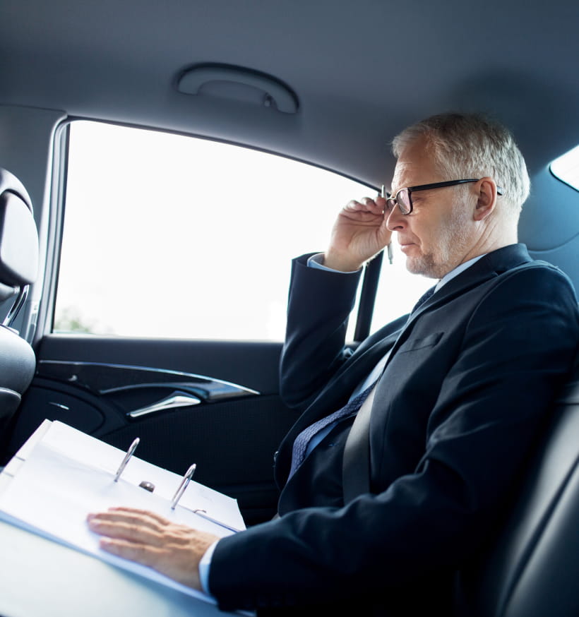 Middle-aged businessman sitting in a luxury sedan, reviewing documents.