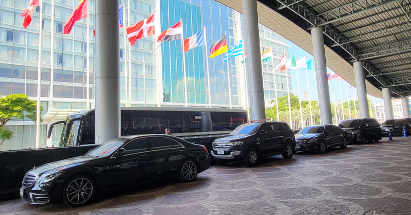 Protocol vehicles, including buses and luxury sedans, lined up waiting under national flags.