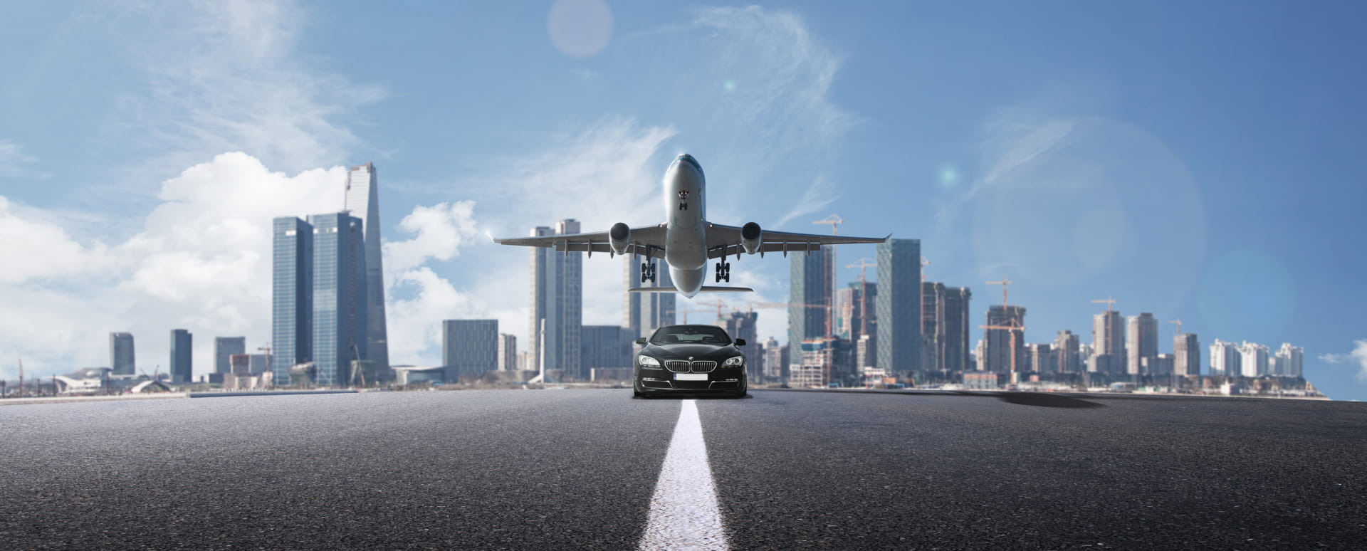 Luxury sedan on the road with a city background and a plane taking off in the sky.