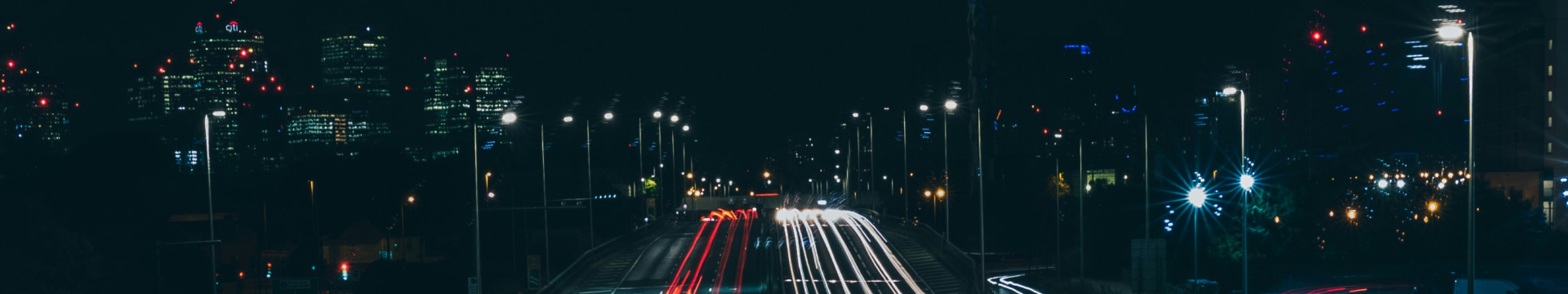 Night view of a highway with light trails from cars and illuminated city buildings in the background.