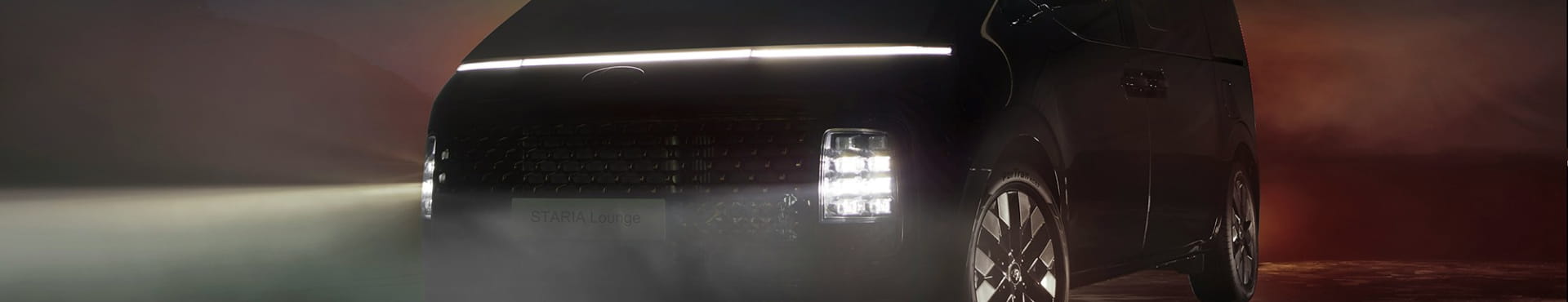 A modern design minivan with its headlights on.