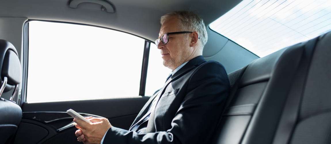 Middle-aged businessman looking at a smartphone in a luxury sedan.